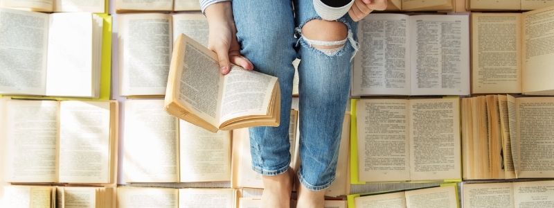 A woman sitting reading a book on top of a pile of open books